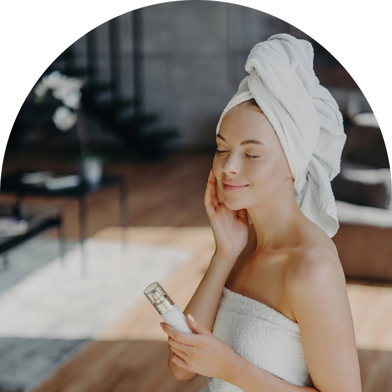 Woman with towel, holding skincare bottle, smiling. Woman with towel, holding skincare bottle, smiling.